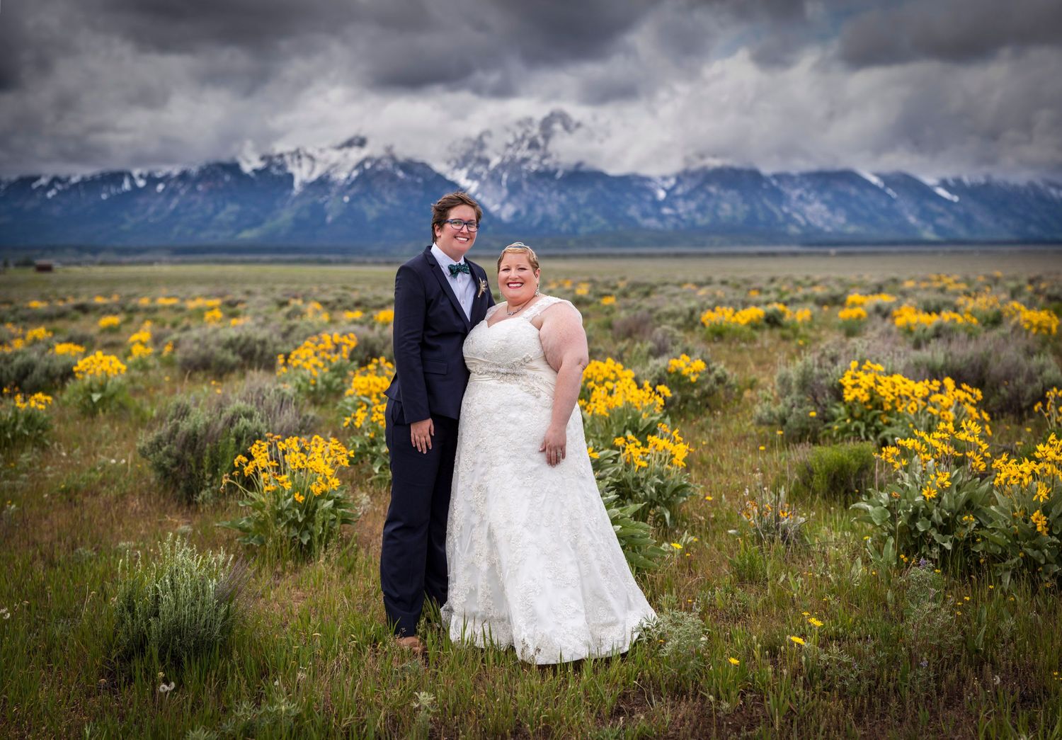 Bride and groom pose in a wildflower meadow with the snow-capped Grand Teton mountains under dramatic skies.