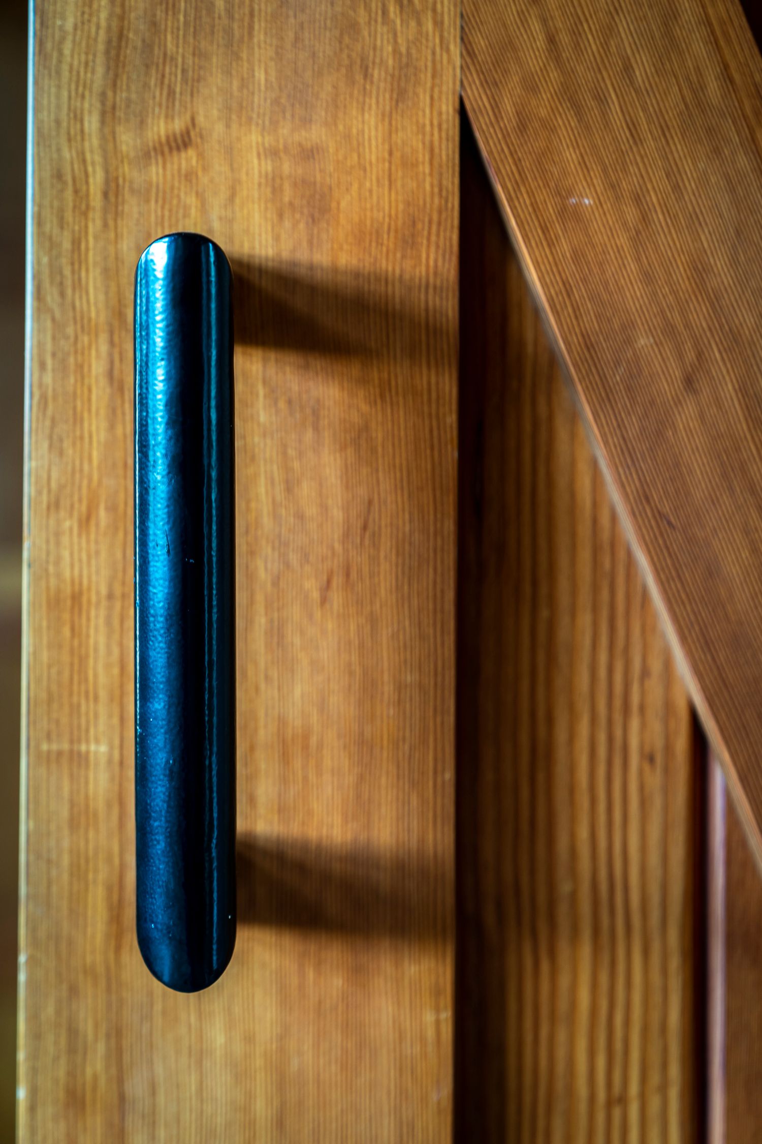 Close-up of a sleek black vertical door handle on a warm wooden cabinet or wardrobe door.