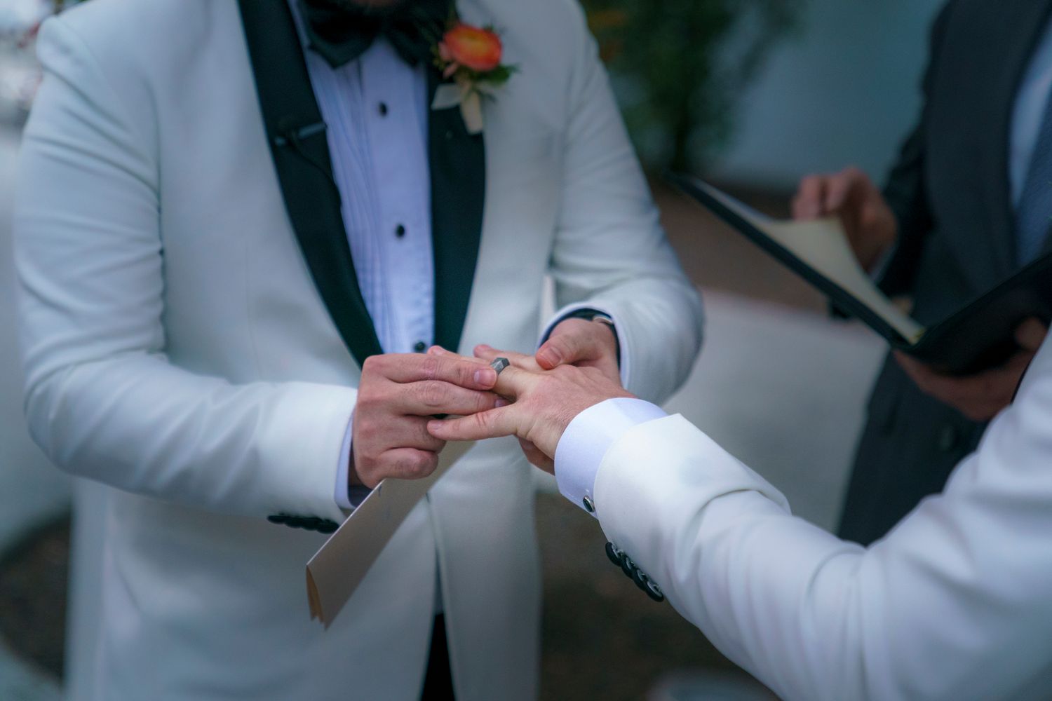 Groom placing a wedding ring on his partners finger during an outdoor wedding ceremony.
