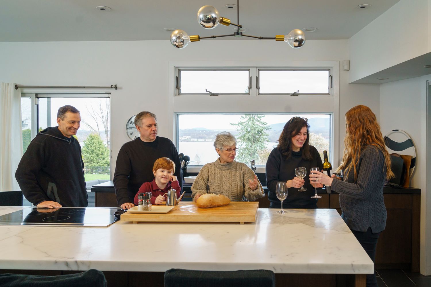 Family gathering around a marble kitchen island, sharing wine and conversation in a modern home.