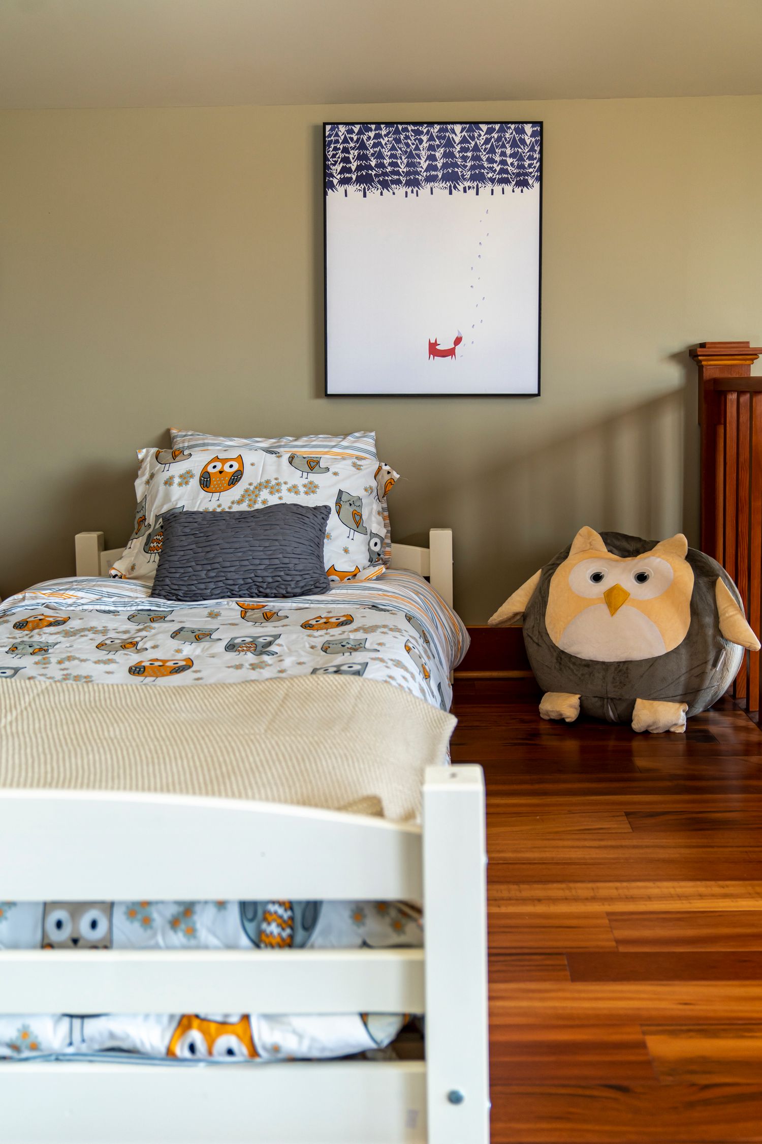 Children's bedroom with owl-themed bedding, stuffed owl toy, hardwood floors, and framed wall art.