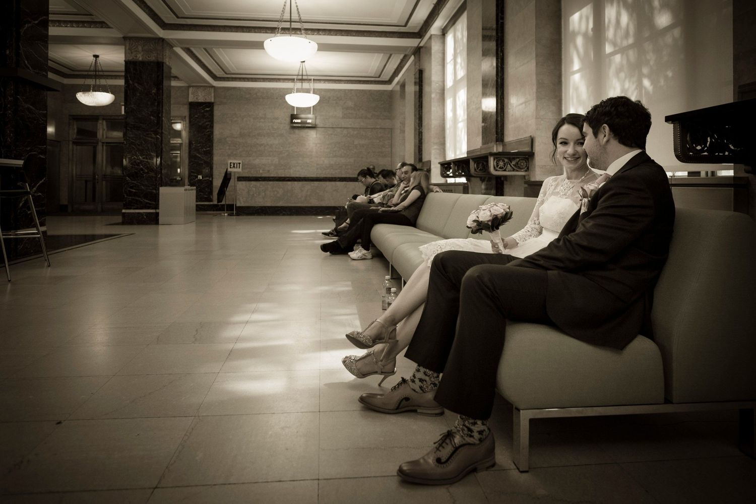 People sitting on benches in a dimly lit lobby, captured in sepia tone.