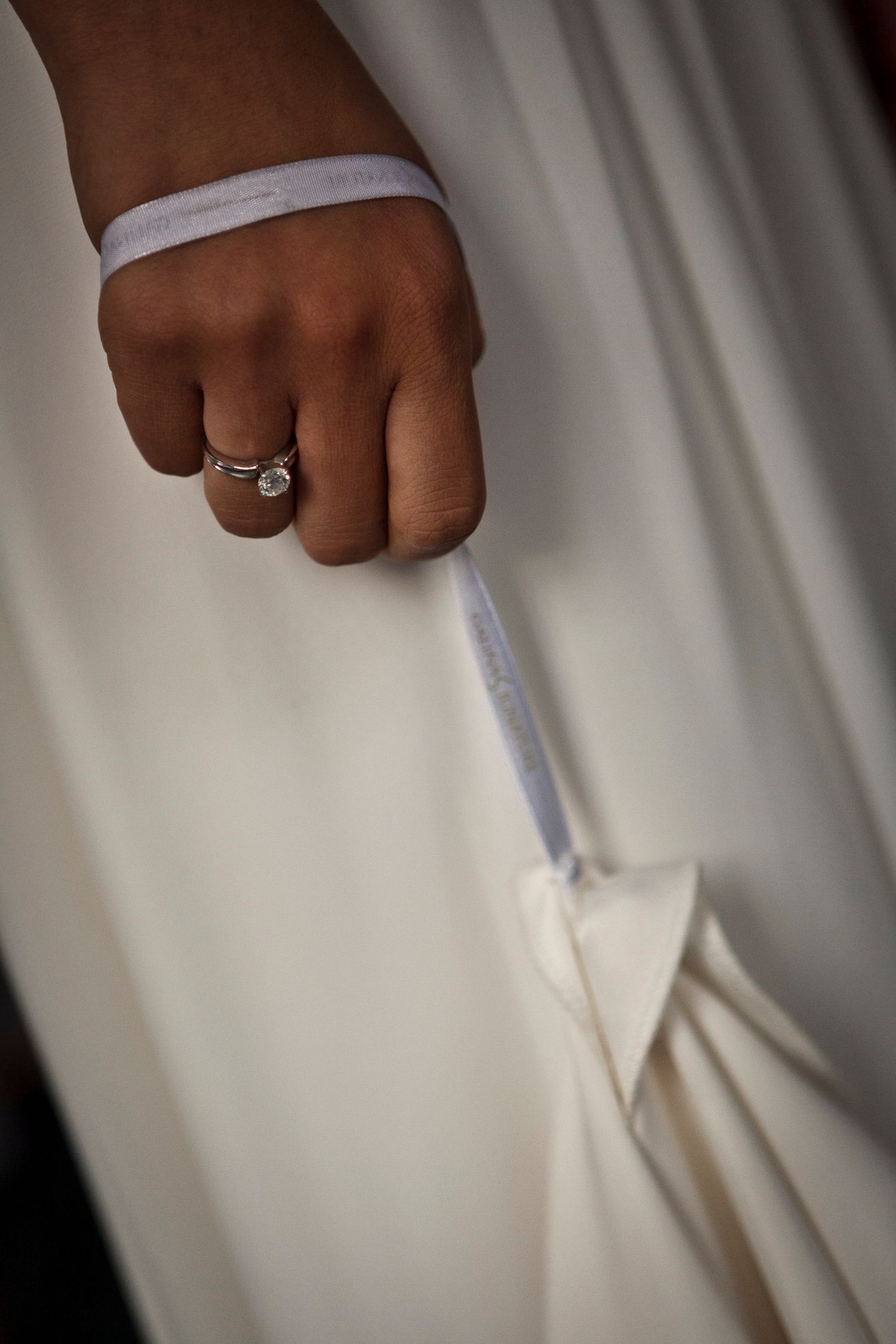 Bride holding wedding dress train revealing diamond engagement ring and white wristband.