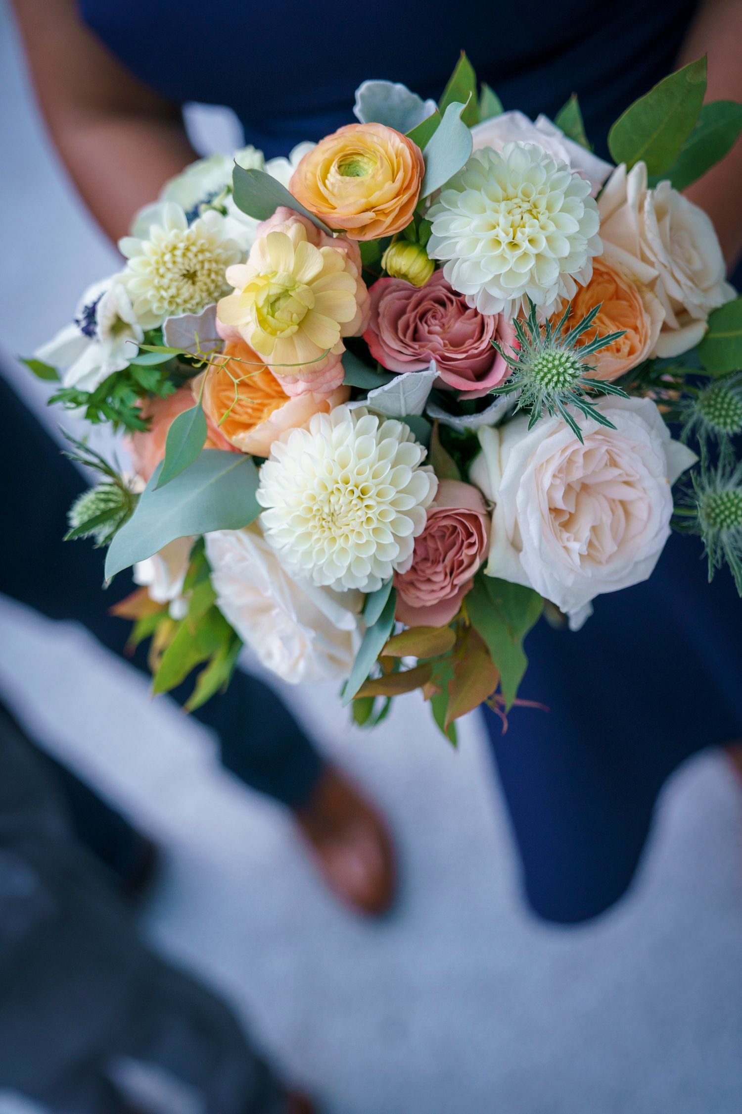 Bride holding elegant wedding bouquet with peach, white, and pink roses, dahlias, and greenery.