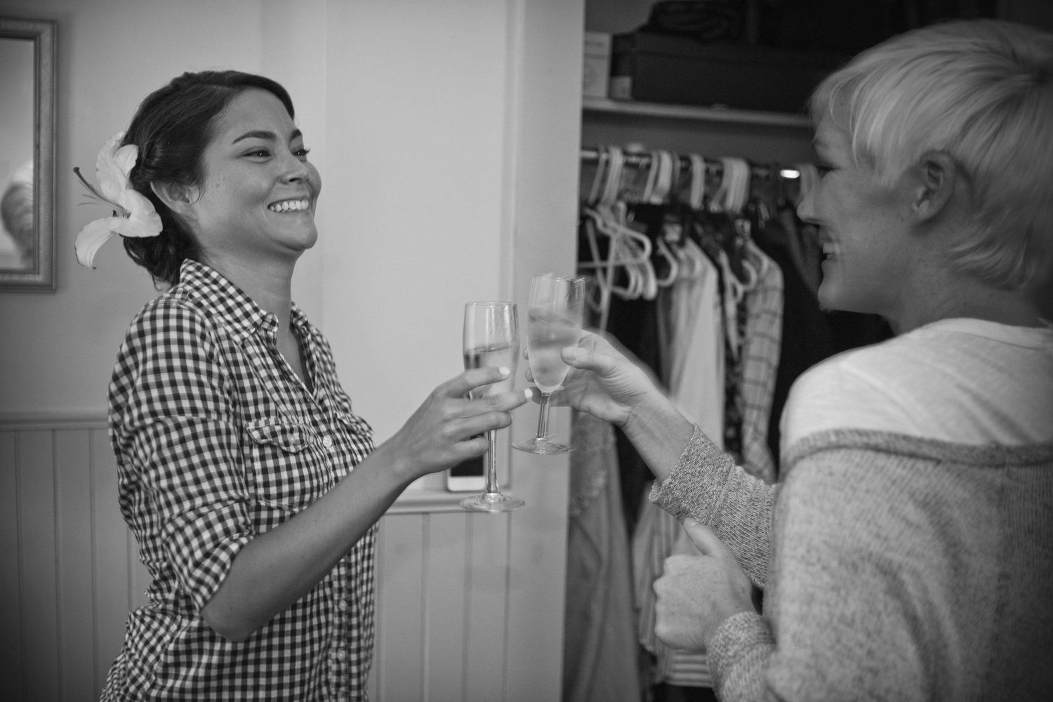 Two women laughing and toasting with champagne glasses in a black and white celebration photo.