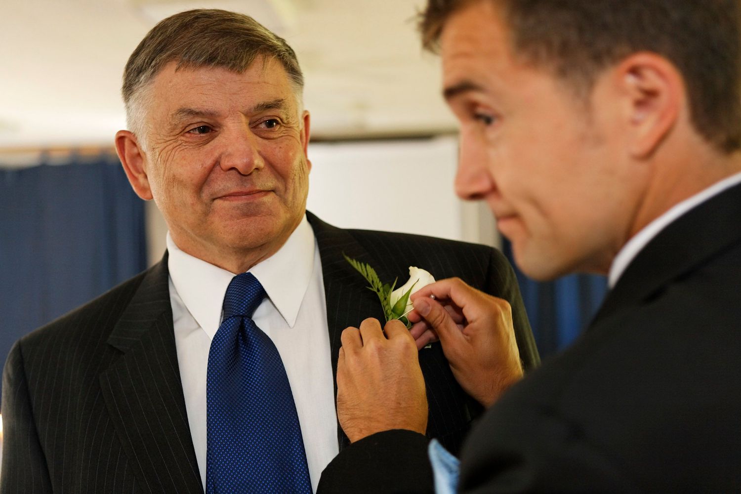 Man in suit with blue tie getting boutonniere pinned on lapel at wedding ceremony.