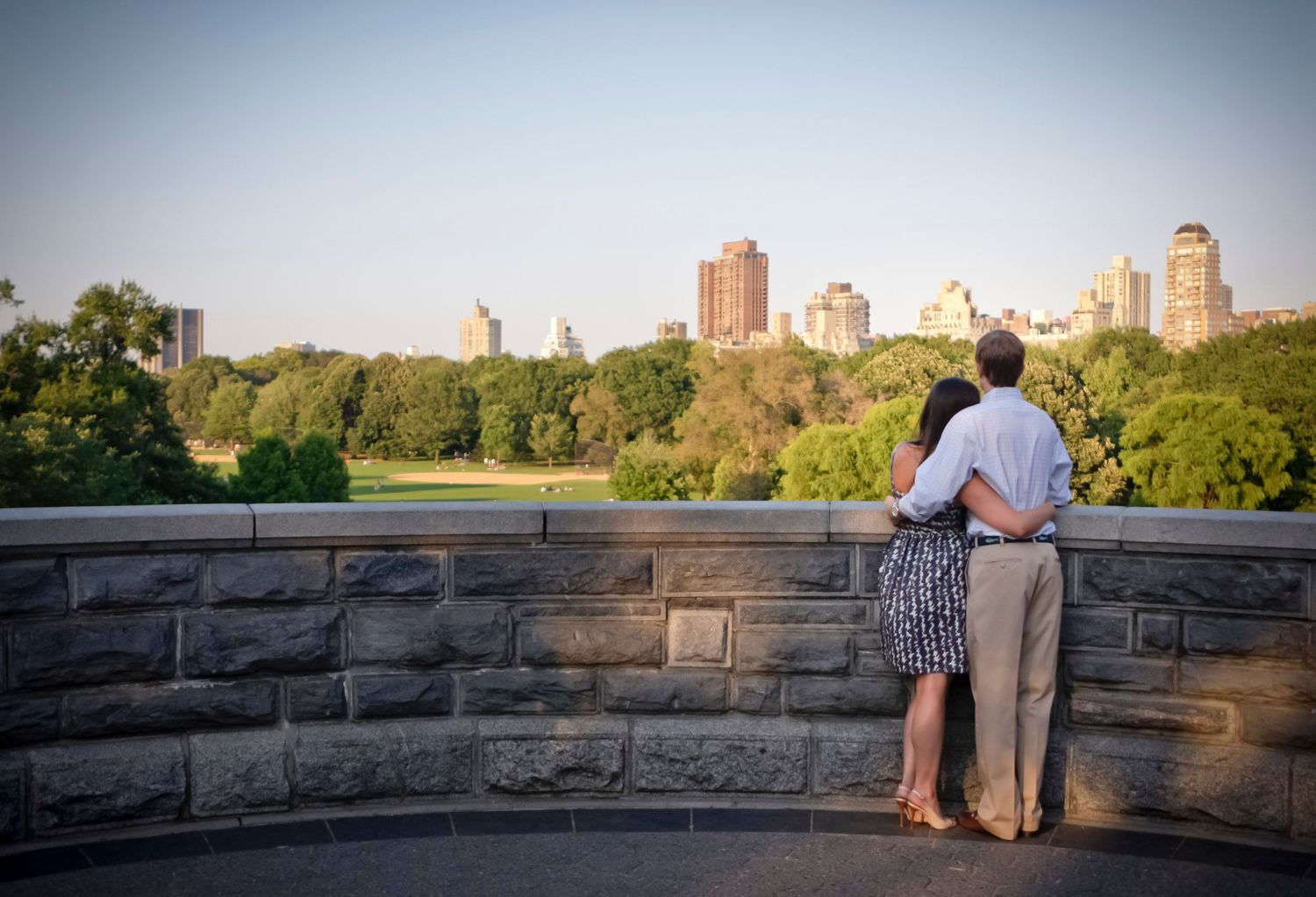 Romantic couple embracing while overlooking Central Park skyline from a stone terrace.