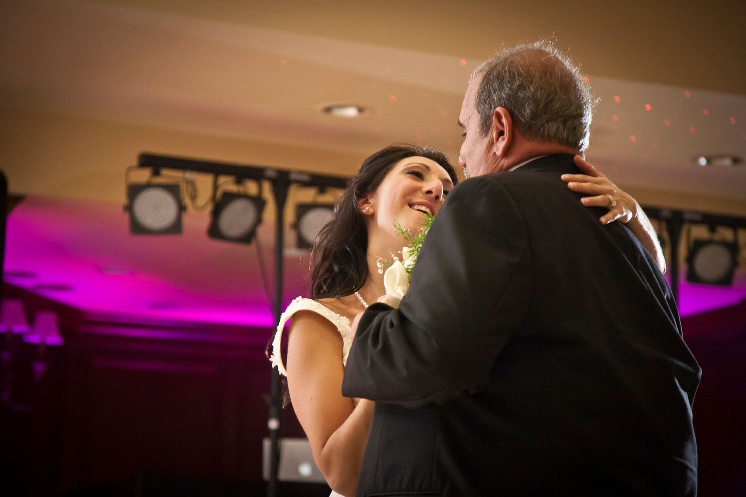 Bride shares emotional father-daughter dance under purple lights at wedding reception.