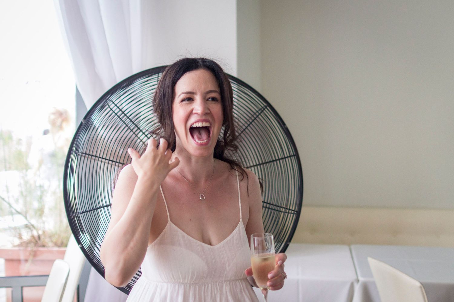 Excited bride in white dress laughing and holding champagne glass at wedding celebration.