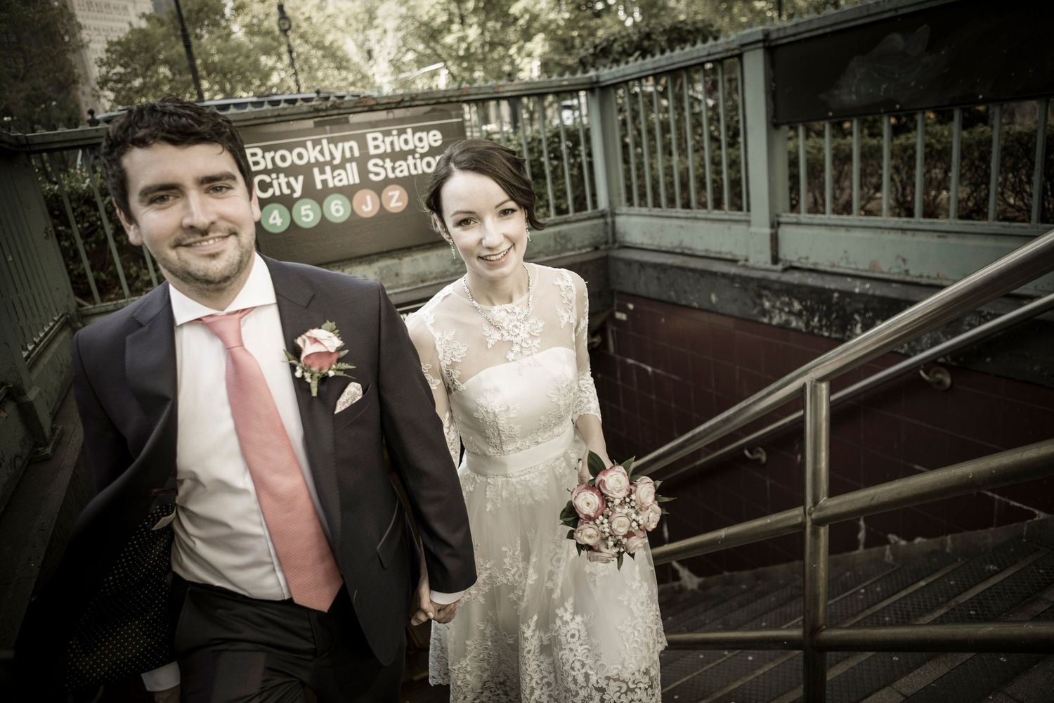 Newlywed couple posing on stairs at Brooklyn Bridge City Hall Station NYC subway entrance on their wedding day.