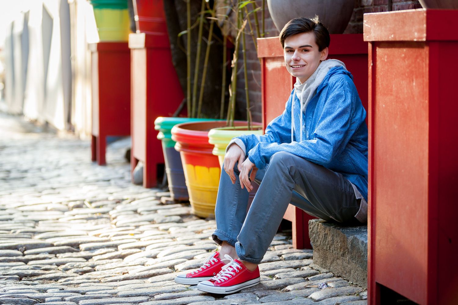 Teen boy in blue hoodie and red Converse sitting on colorful cobblestone steps.