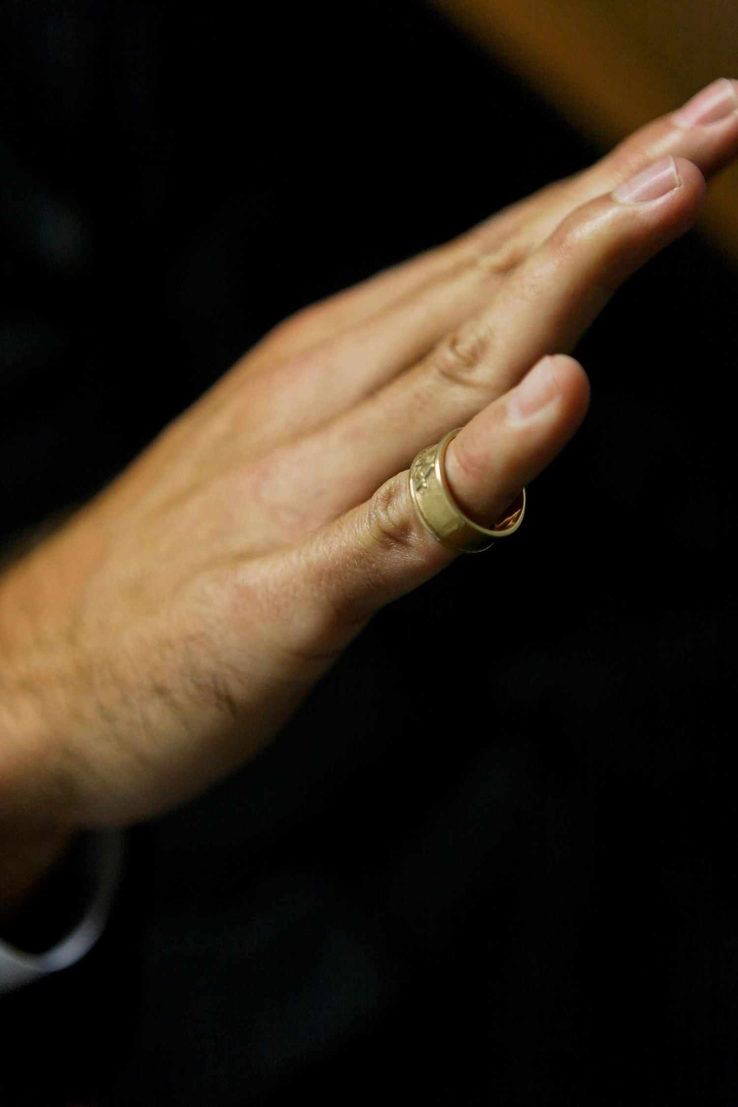 Close-up of groom's hand displaying gold wedding band ring against dark background.