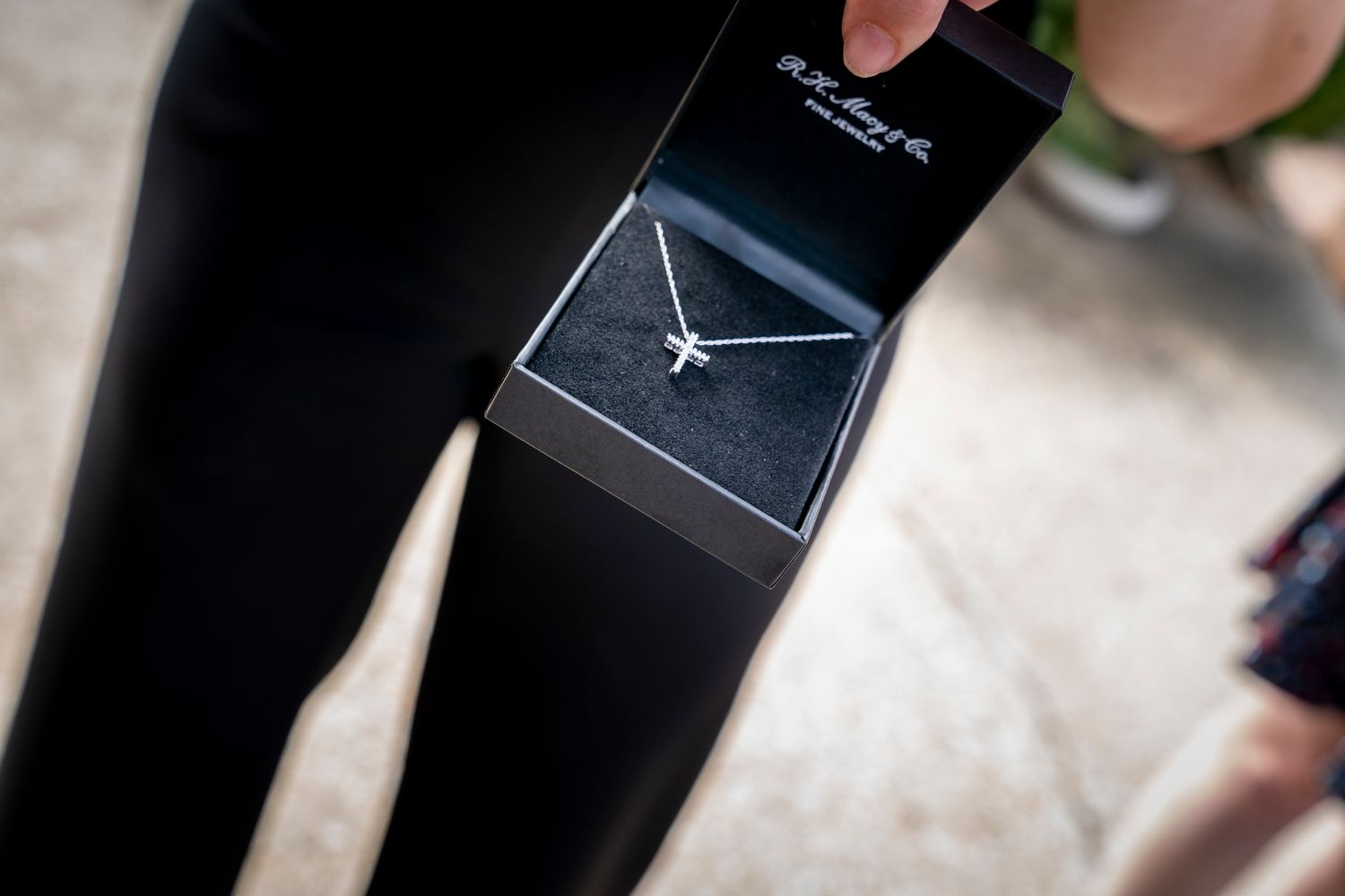 Silver airplane pendant necklace displayed in a black gift box, held by a person wearing black leggings.