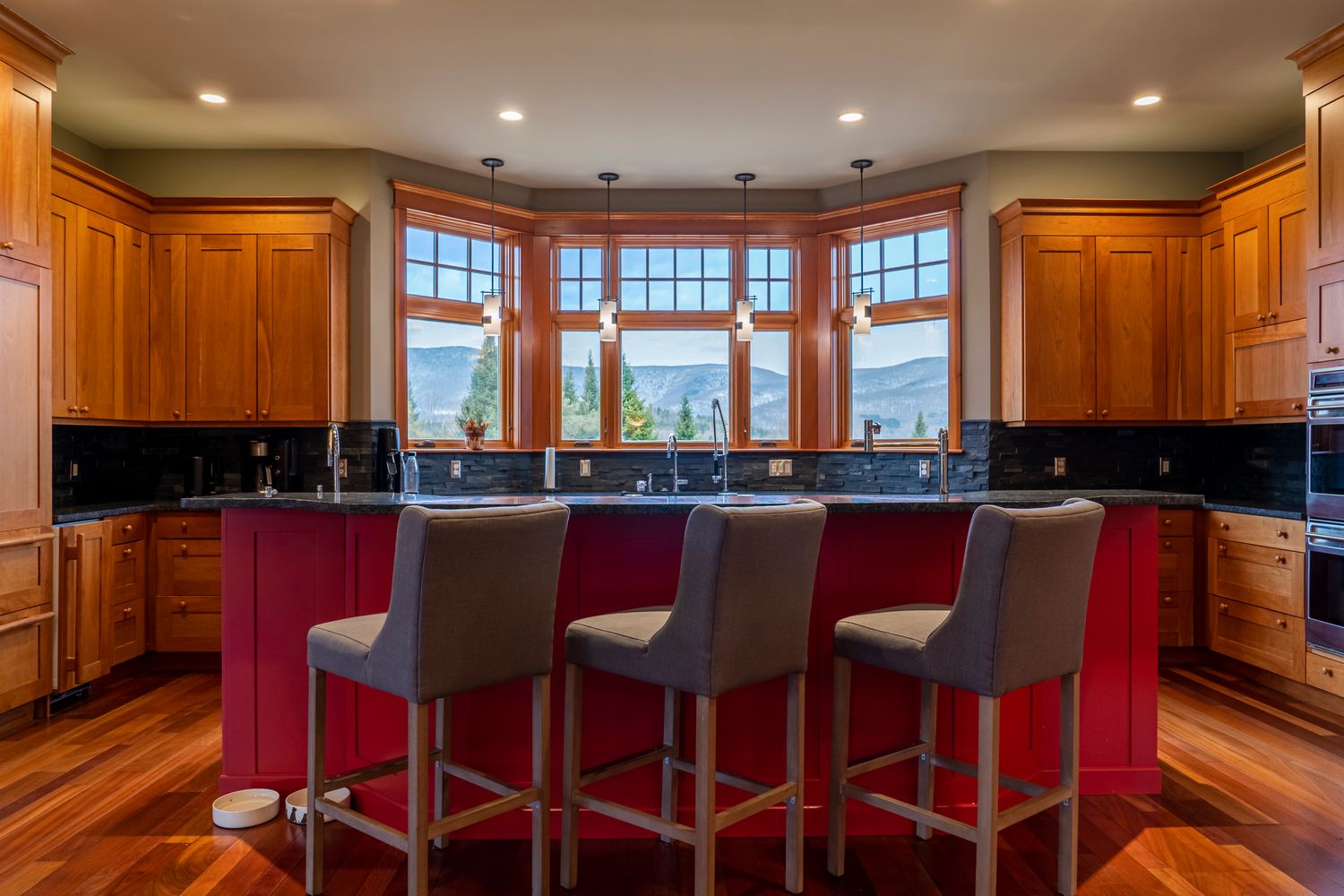 Elegant kitchen with red island, gray bar stools, honey oak cabinets, black granite countertops, and bay windows.