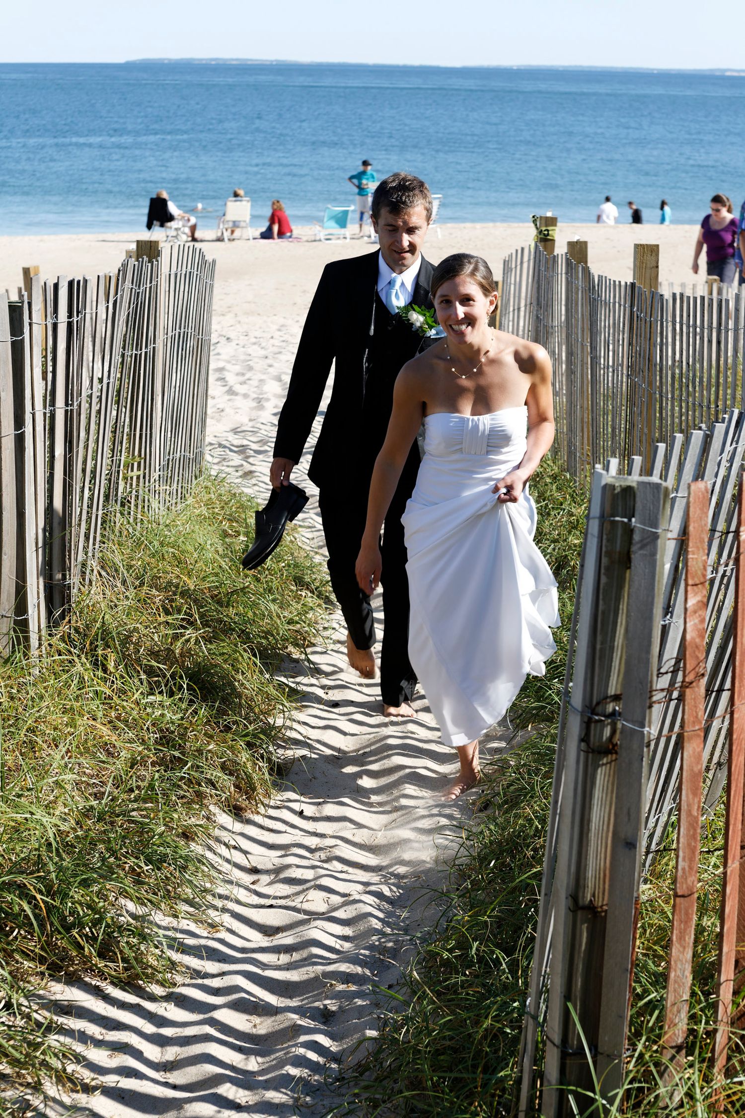 Bride and groom walking hand in hand up sandy beach path.