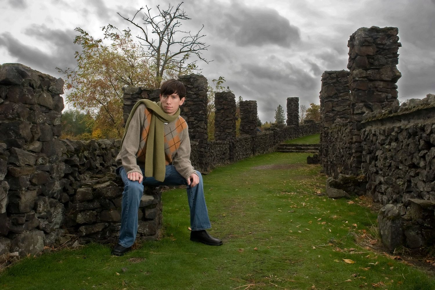 Young man sitting on ancient stone ruins under dramatic cloudy autumn sky.