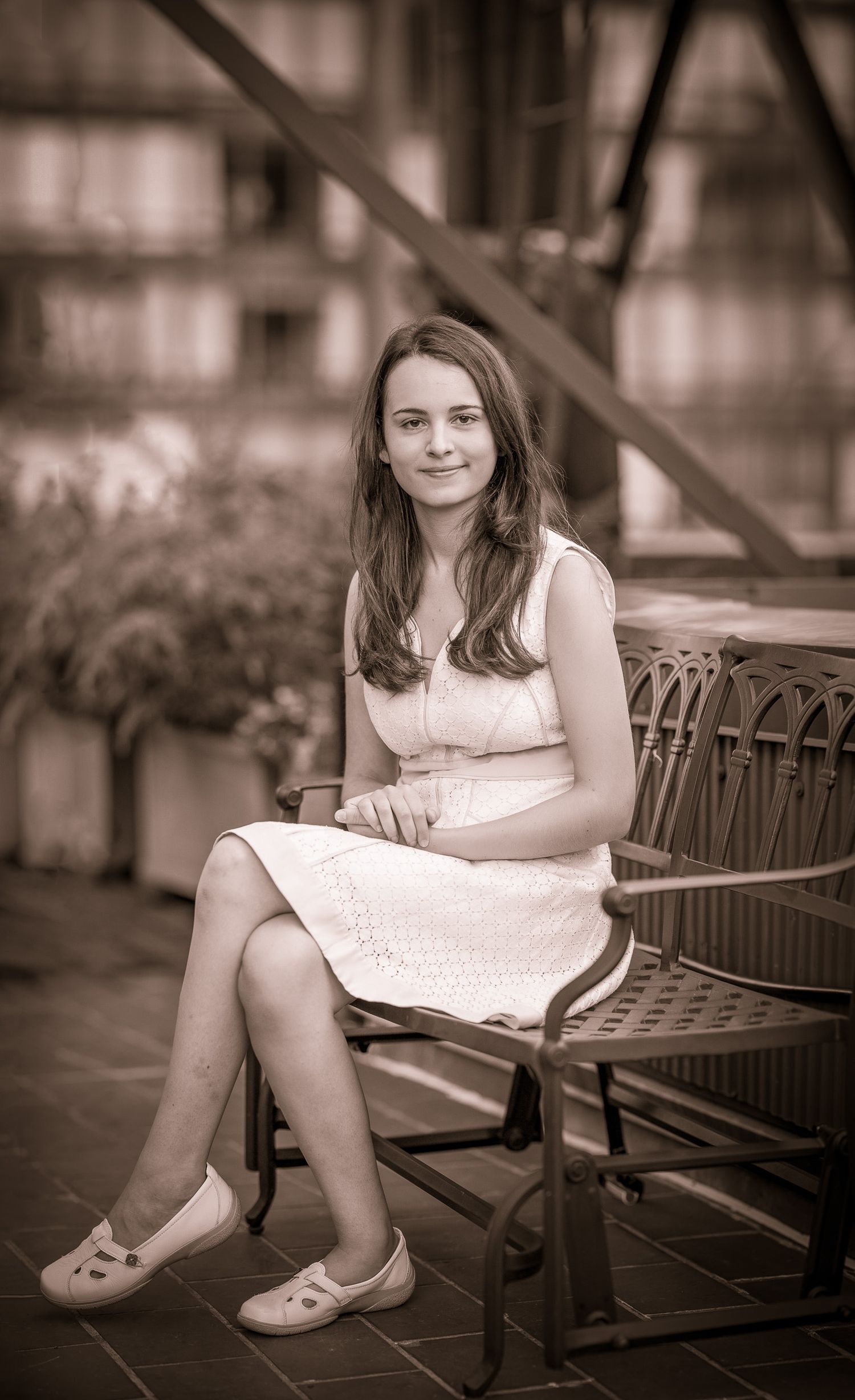Young girl in white dress seated on bench in sepia-toned portrait.