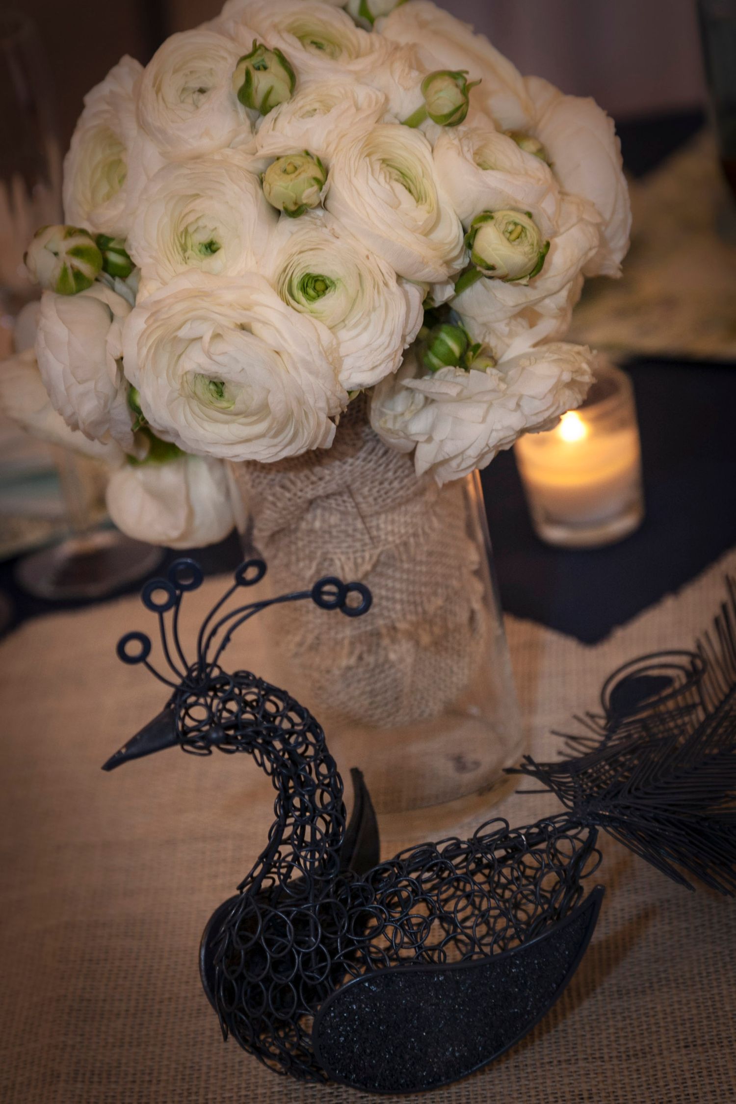 White ranunculus bouquet in burlap vase beside black wire swan wedding centerpiece.