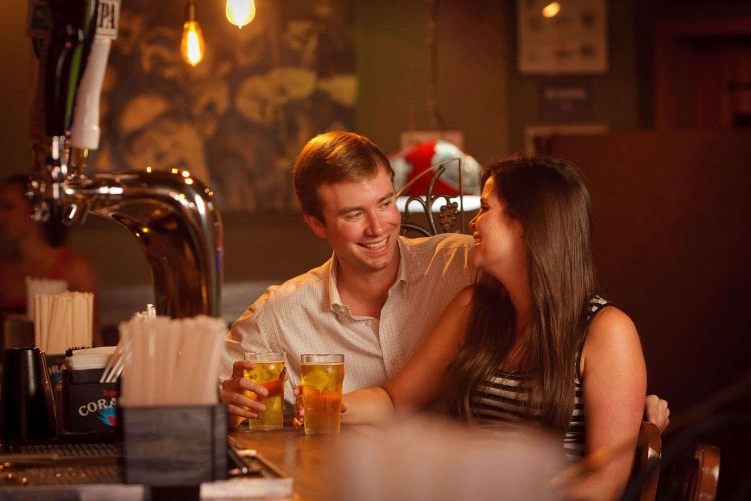 Young couple sharing a romantic moment over drinks at a warmly lit bar counter.