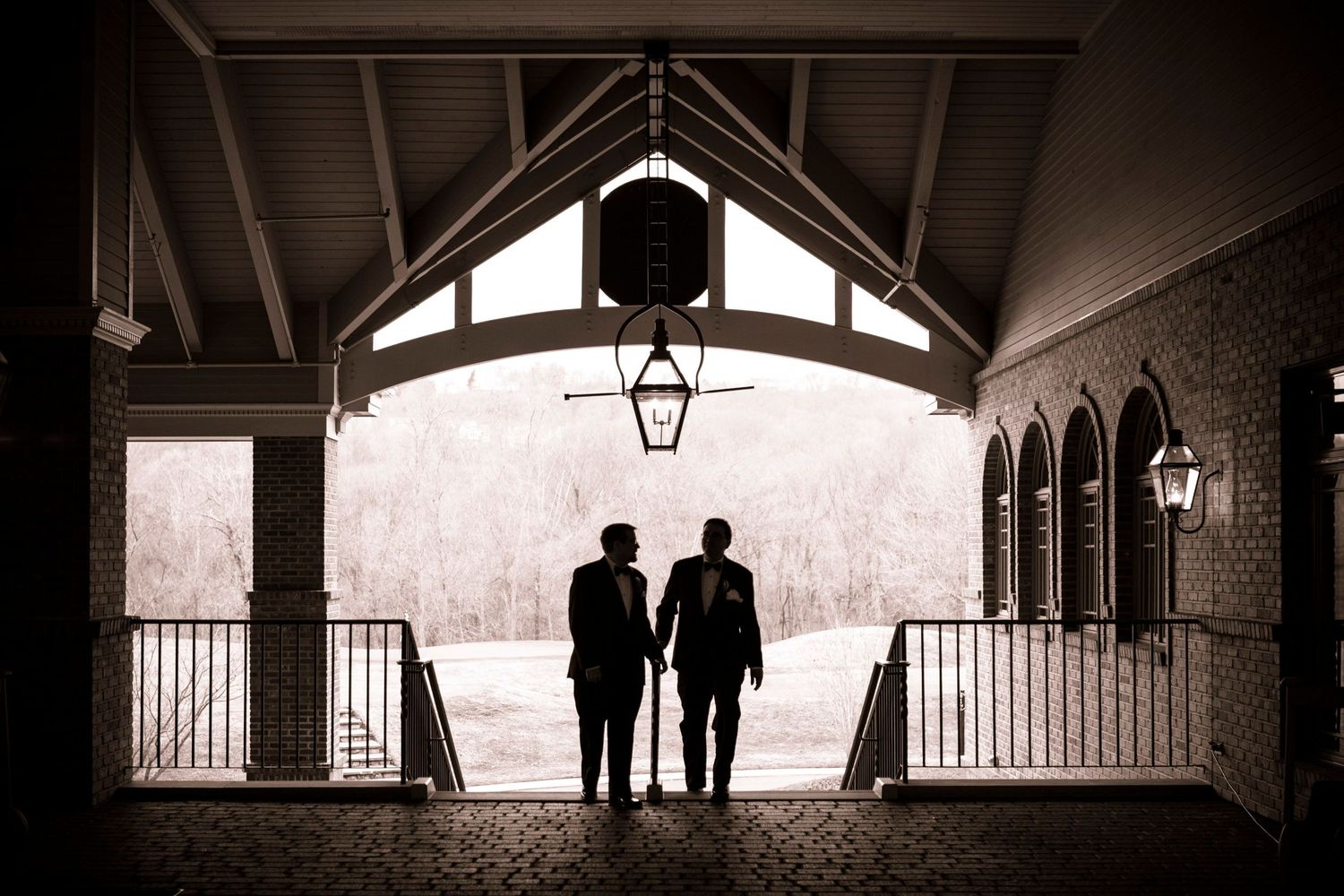 Silhouette of two grooms holding hands under an elegant venue archway on their wedding day.