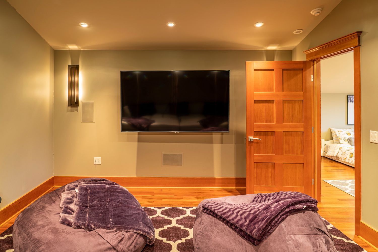 Cozy media room with wall-mounted flat-screen TV, purple bean bag chairs, and hardwood floors.