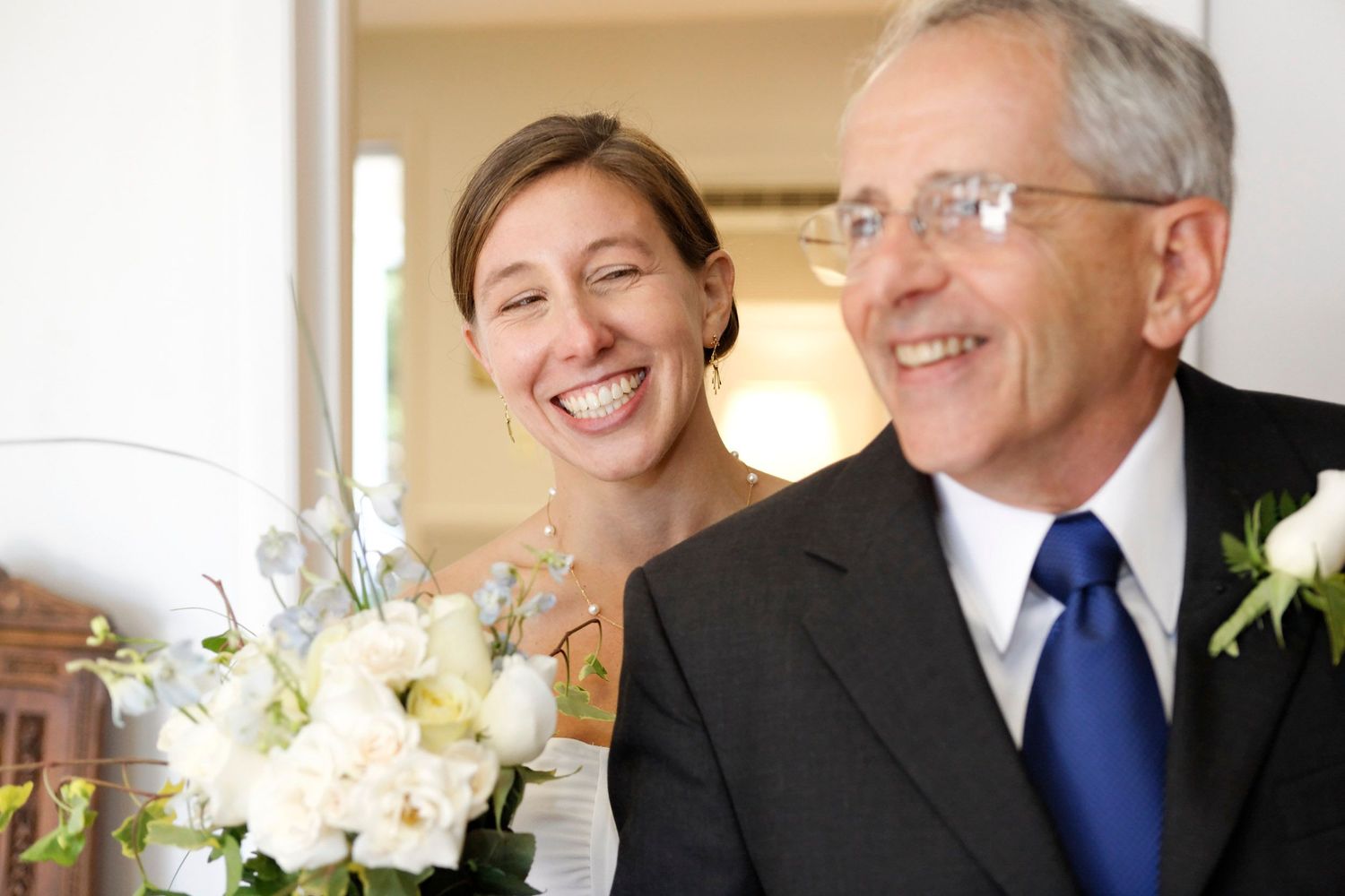 Happy bride with white bouquet standing beside older man in suit at wedding.