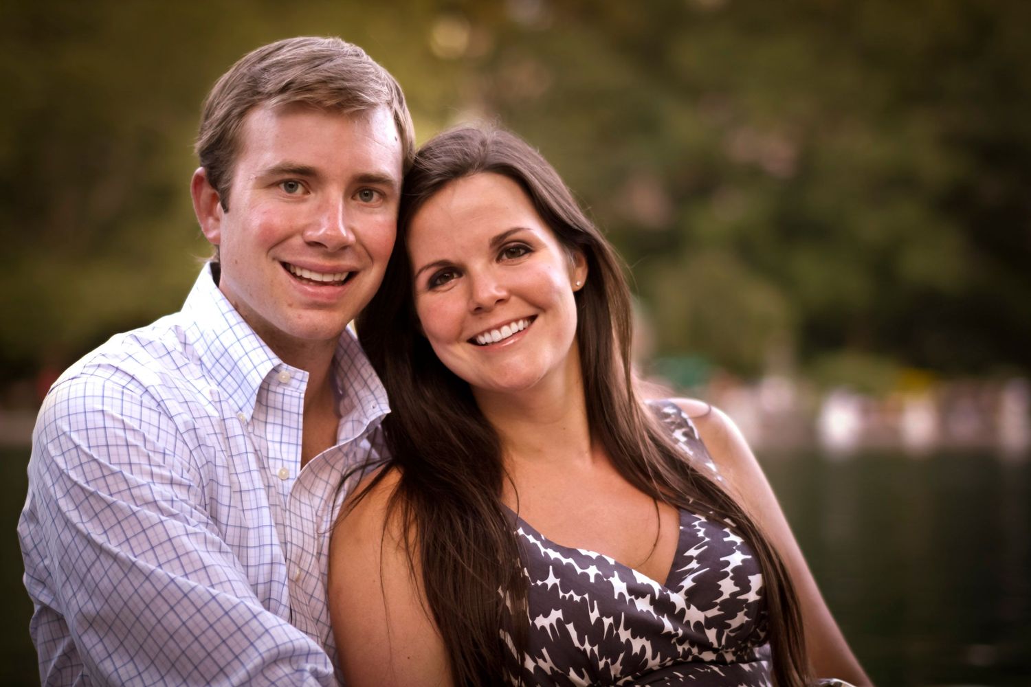 Cheerful couple smiling closely together outdoors near a pond with soft natural lighting.