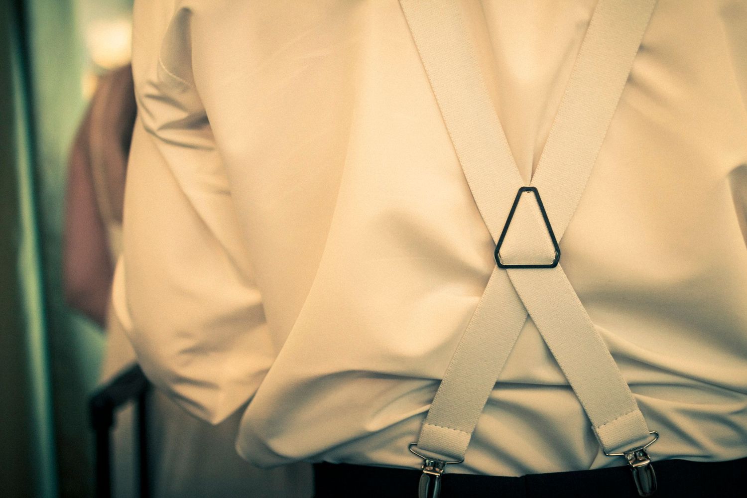 Close-up of groom wearing white shirt with suspenders at a wedding.