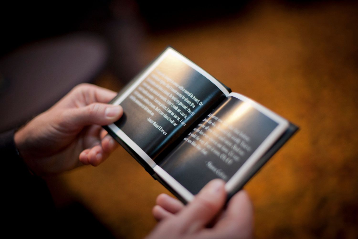 Hands holding an open wedding program booklet with elegant text on dark background pages.