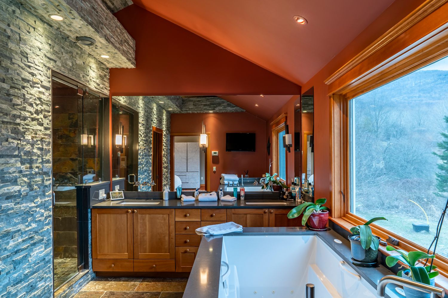 Luxurious master bathroom with stone accent wall, wood vanity, soaking tub, and large window with mountain views.