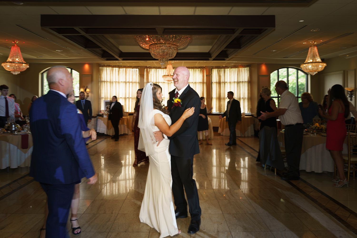 Bride and older gentleman share a father-daughter dance in an elegant chandelier-lit wedding reception ballroom.