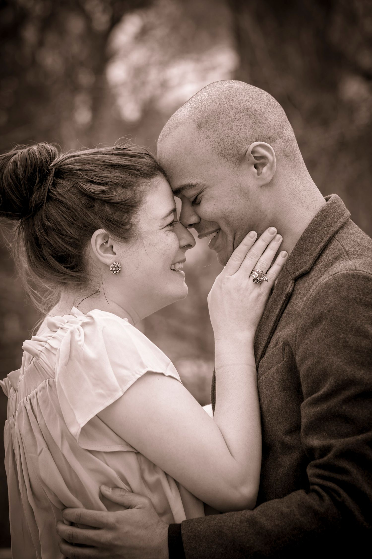 Black and white photo of a smiling couple touching foreheads, woman in white dress with ring, man in gray suit jacket.