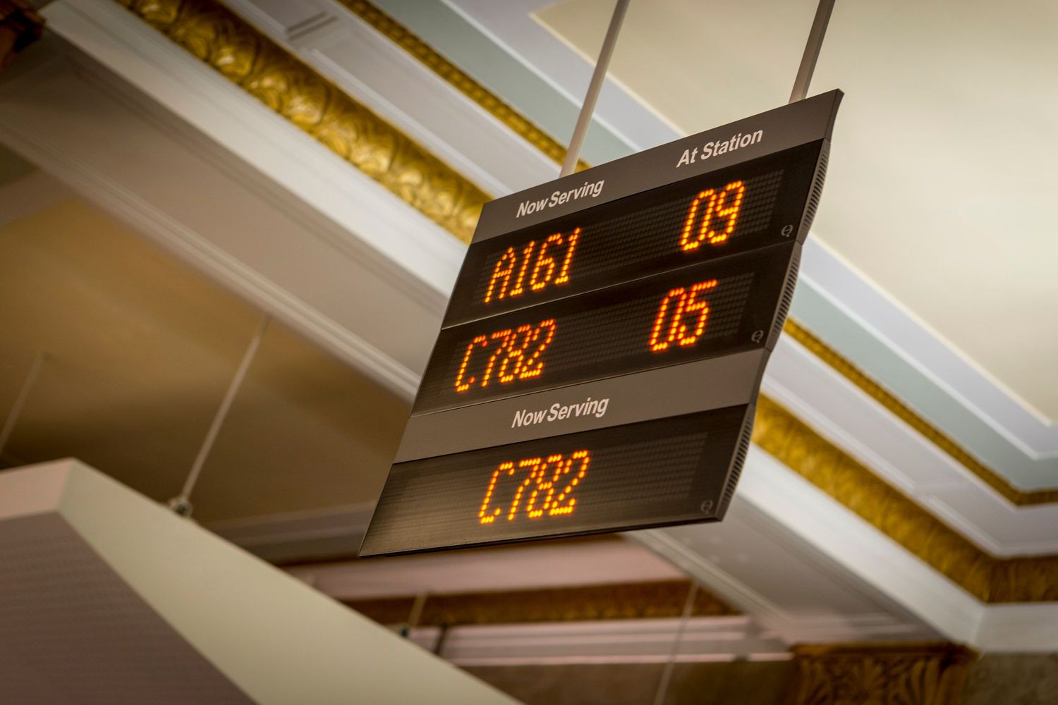 Digital queue display board showing ticket numbers A161, C782 at service stations 09 and 05 in a waiting area.