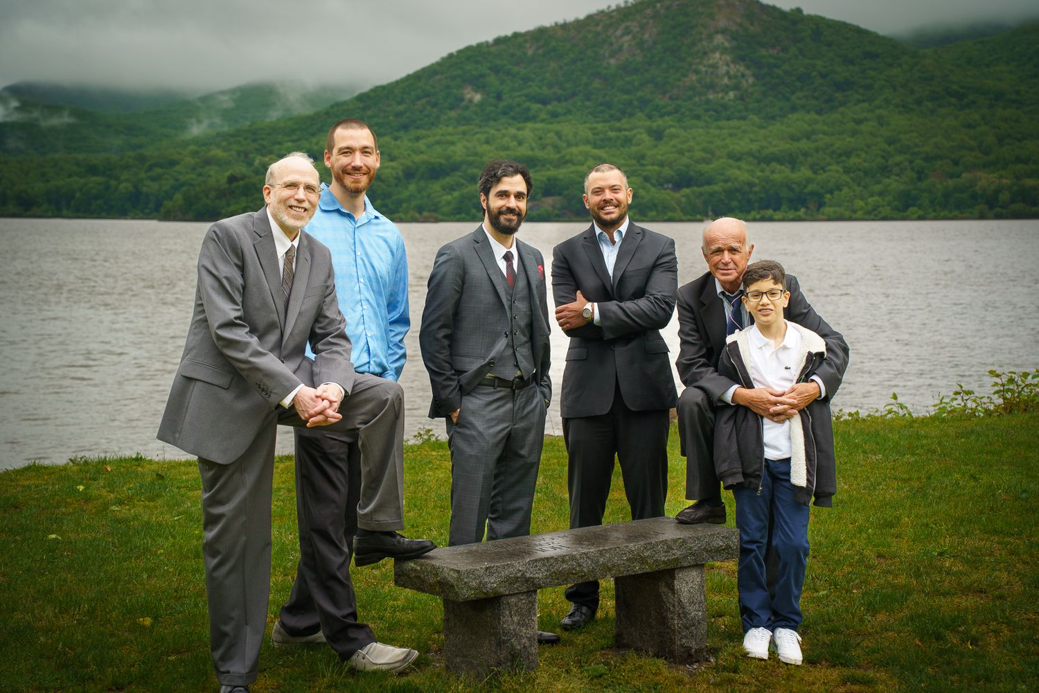 Group of men and a boy posing outdoors near a lake with a scenic mountain backdrop.