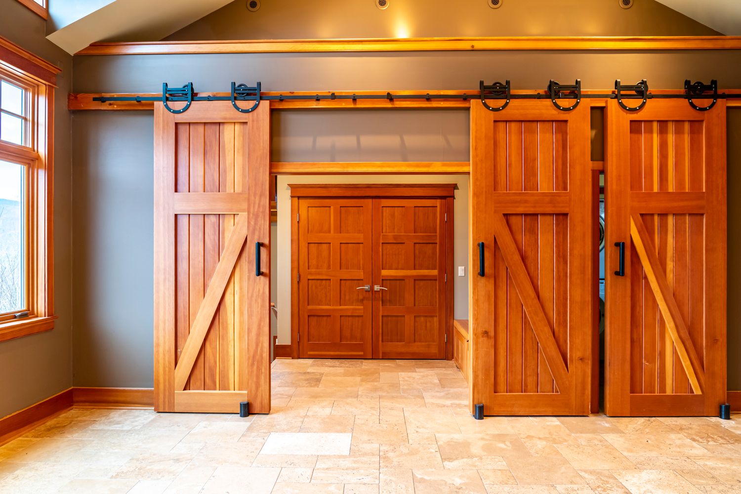Rustic interior with sliding barn doors on a rail system, featuring natural wood panels and stone tile flooring.