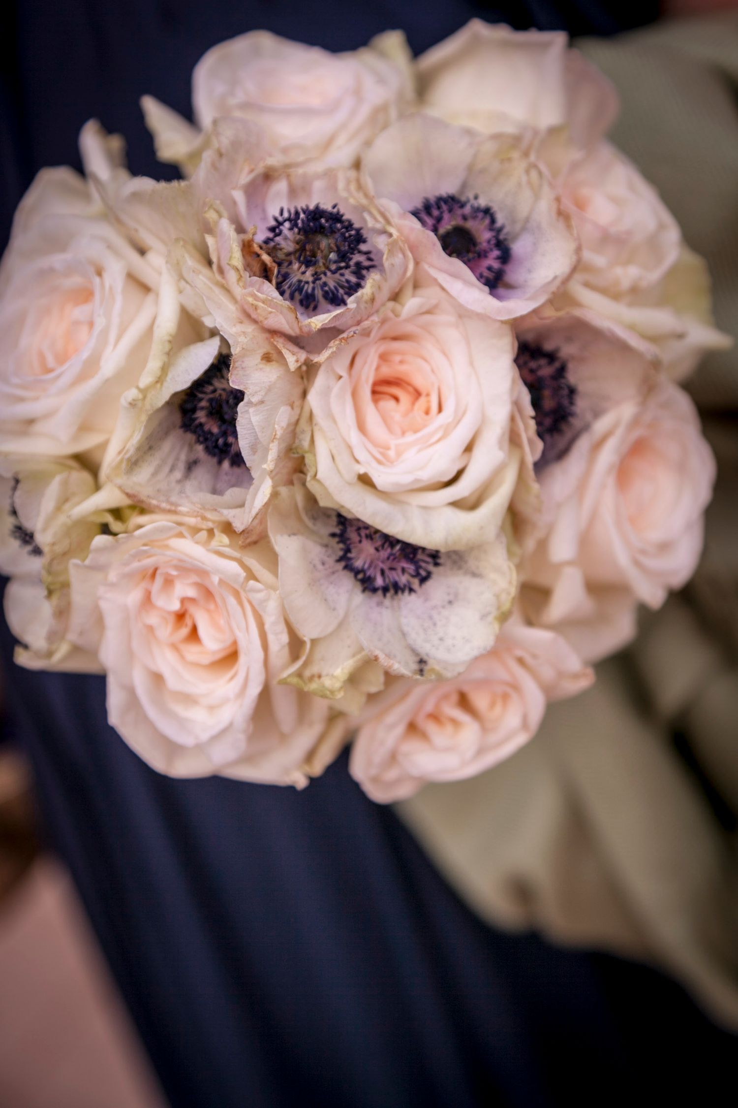 Bridal bouquet of blush pink roses and purple anemones held by bridesmaid.