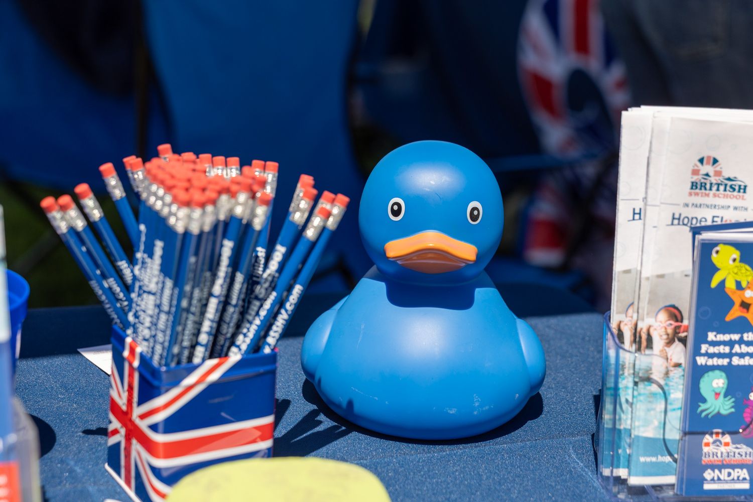 Blue rubber duck and British flag pencil holder on a table at a British swimming event.