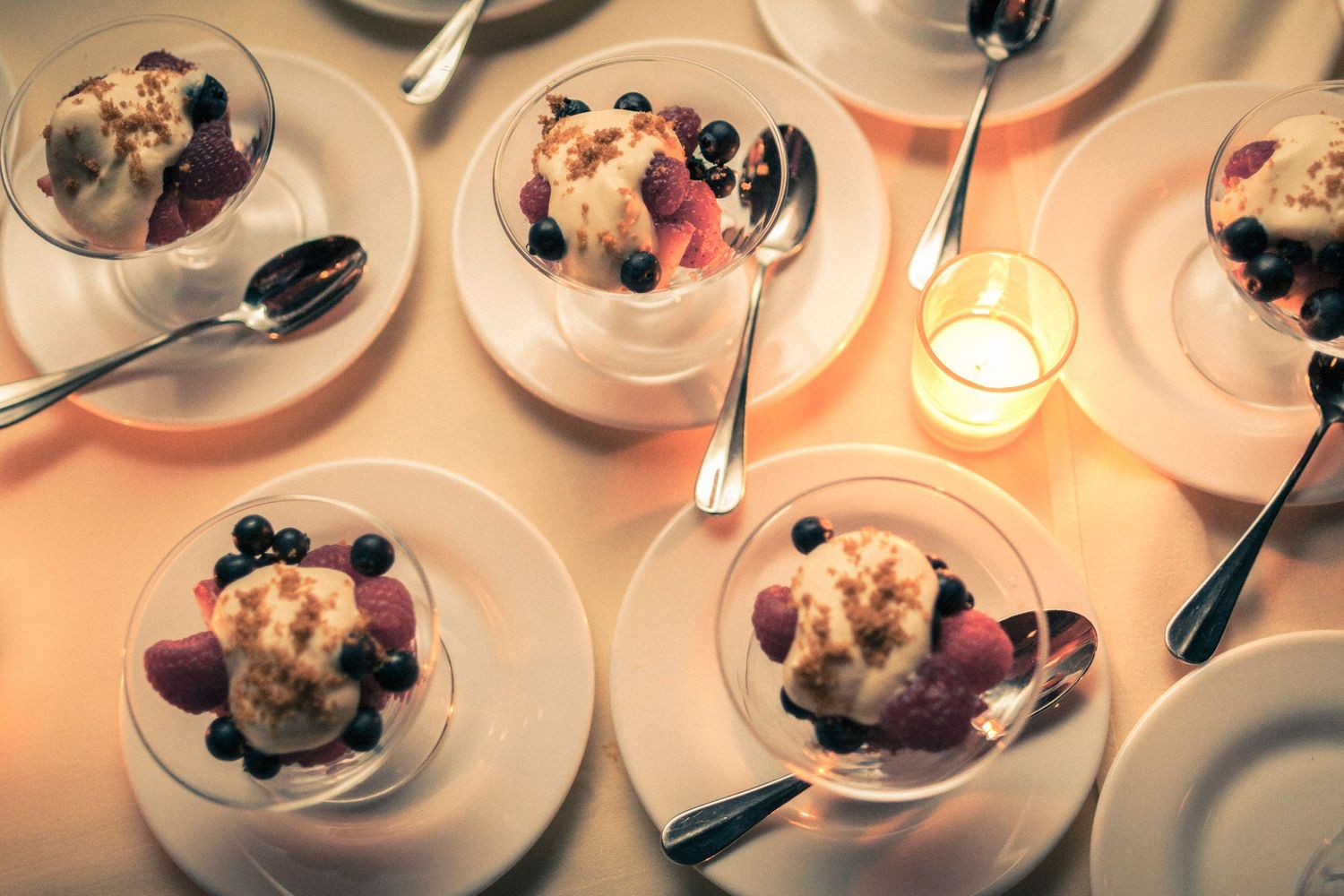 Elegant dessert cups with ice cream and fresh berries served on white plates by candlelight at a dinner party.