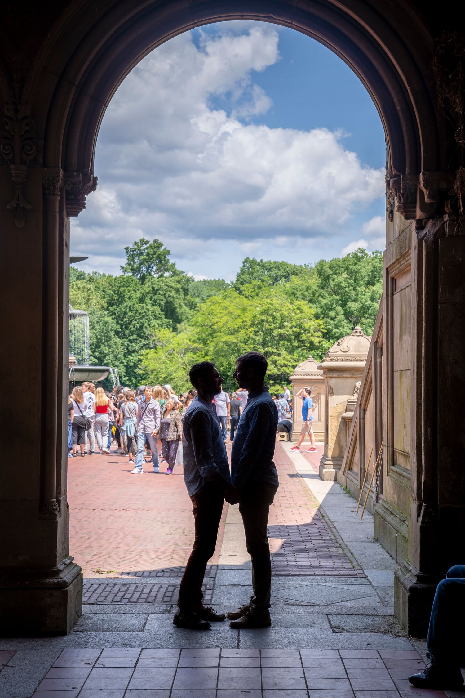 Two people silhouetted in a stone archway at Bethesda Terrace, Central Park, NYC, sharing a romantic moment.