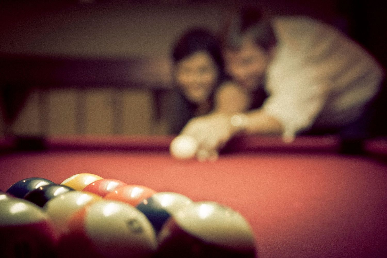 Couple playfully leaning over a red billiard table focused on a rack of pool balls.