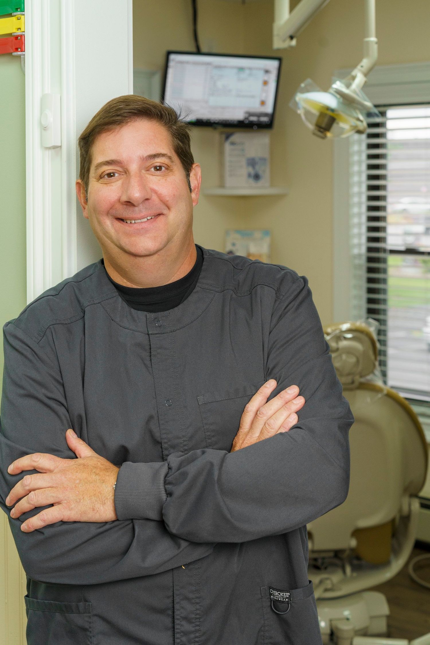 Smiling male dental professional in scrubs posing in a modern dental office.