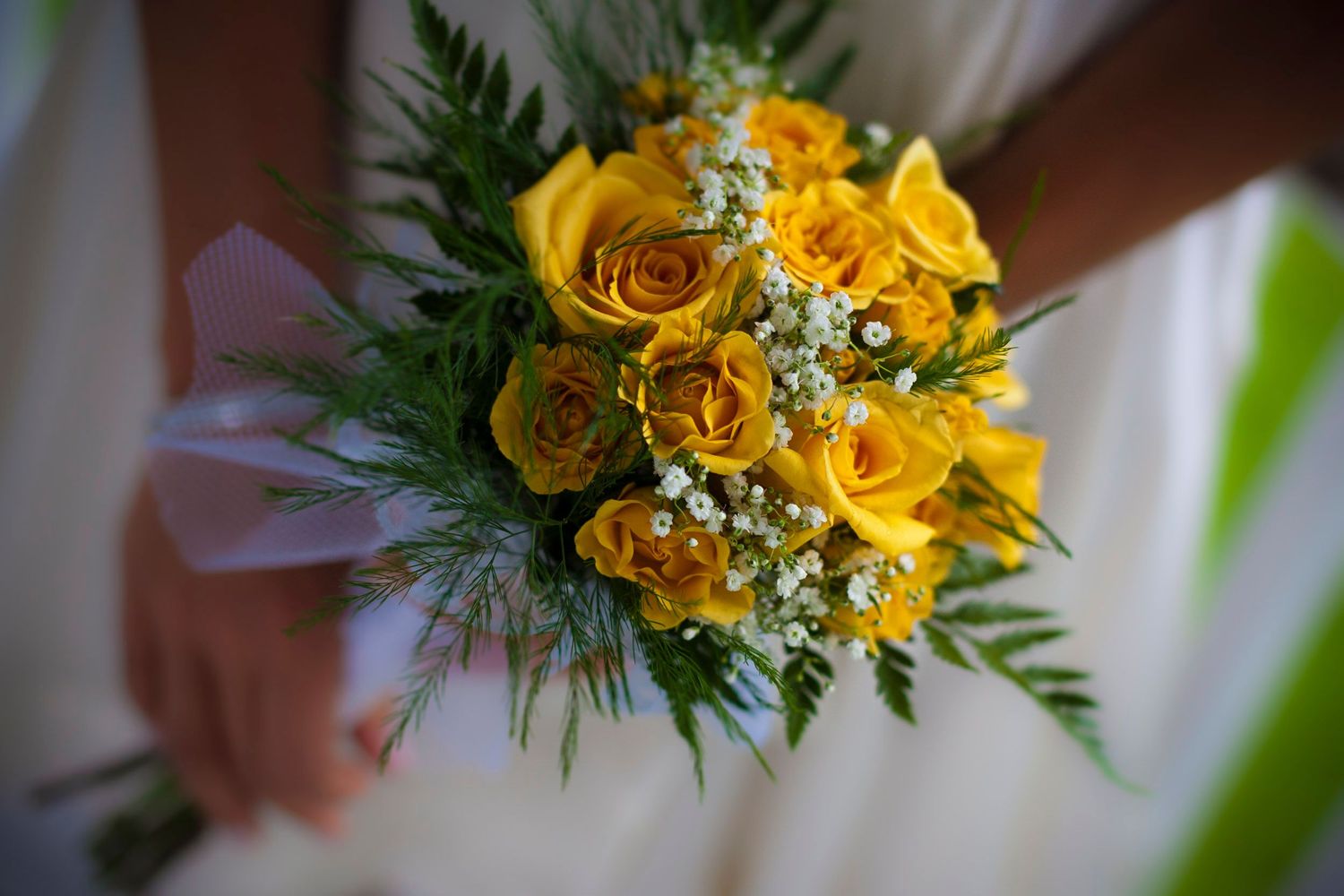 Bride holding a vibrant bouquet of yellow roses and baby's breath on her wedding day.