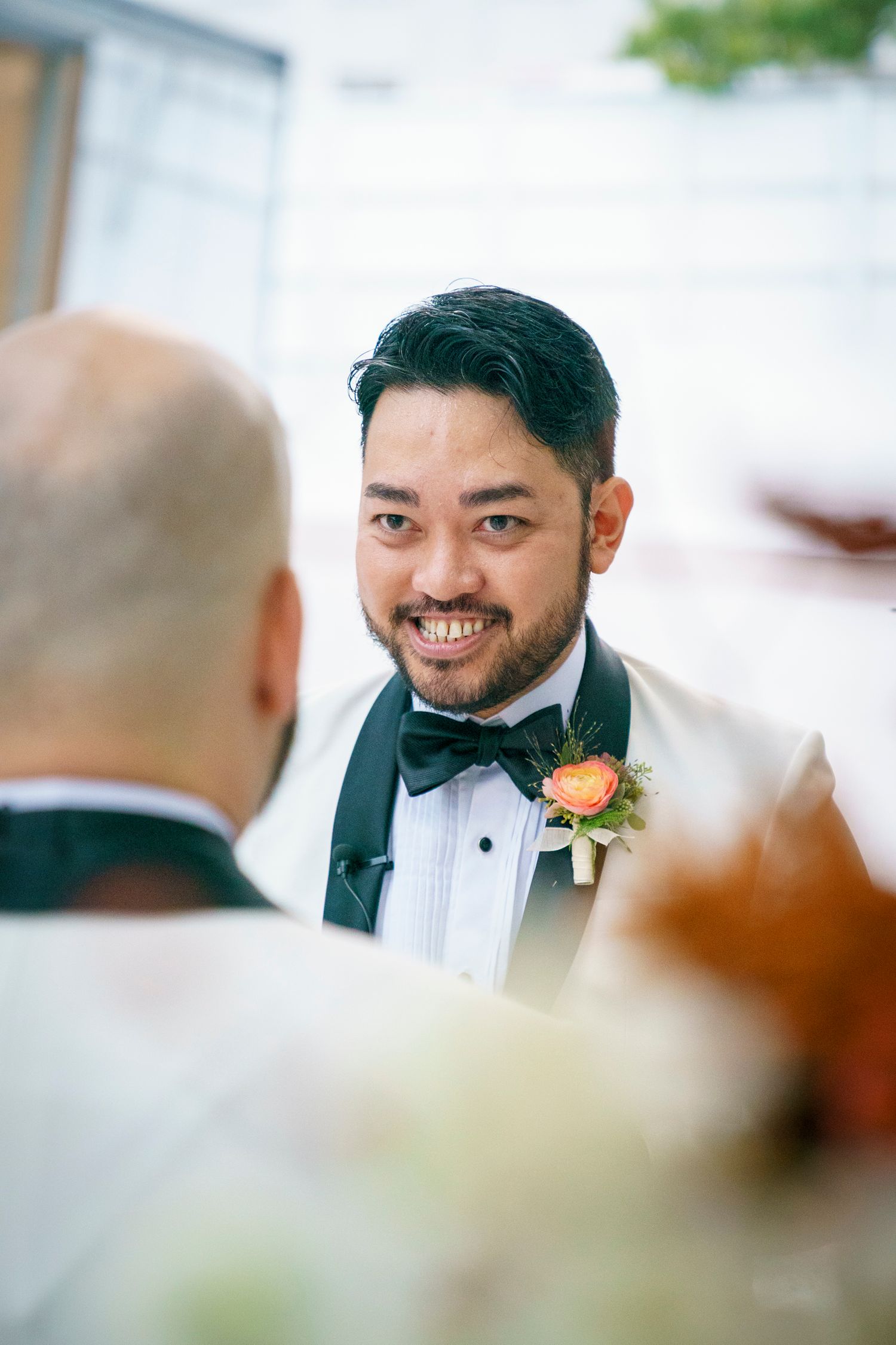 A smiling groom in a white tuxedo with a floral boutonniere stands at the wedding ceremony altar.