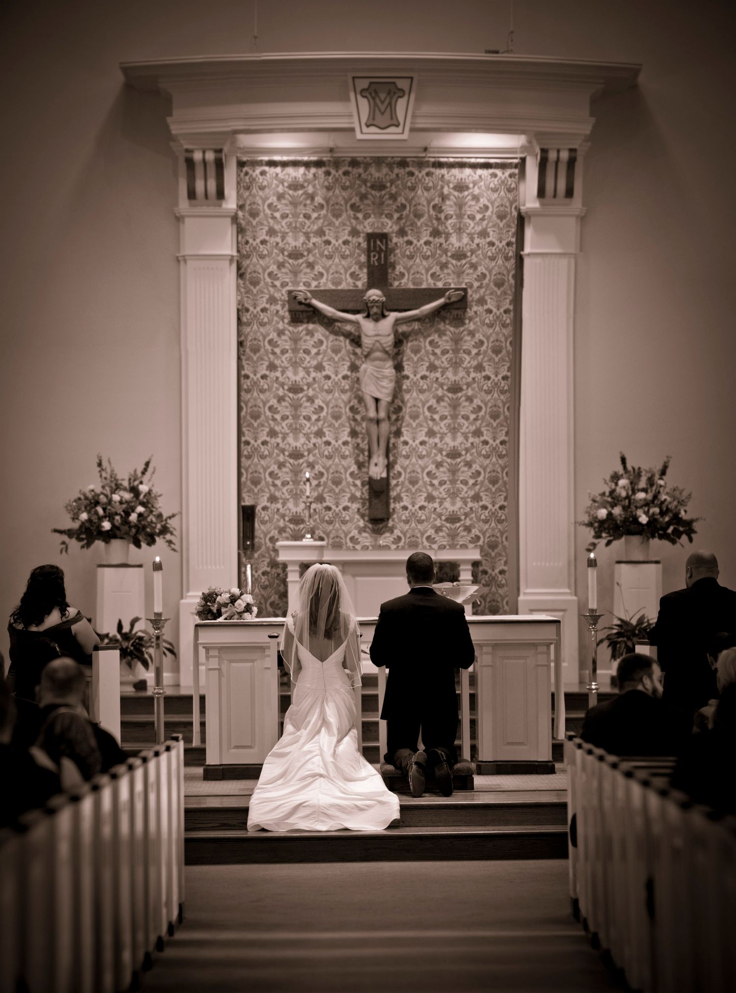 Bride and groom kneeling at church altar before crucifix during Catholic wedding ceremony.