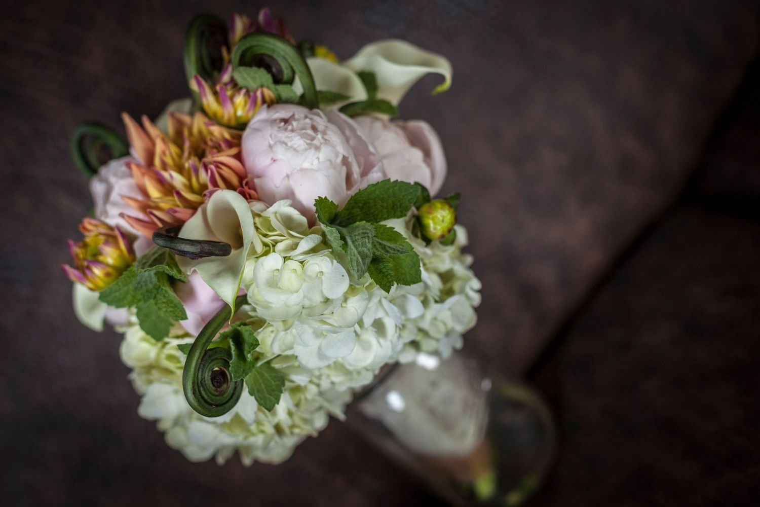 Elegant bridal bouquet with pink peonies, white hydrangeas, and green accents in a glass vase.