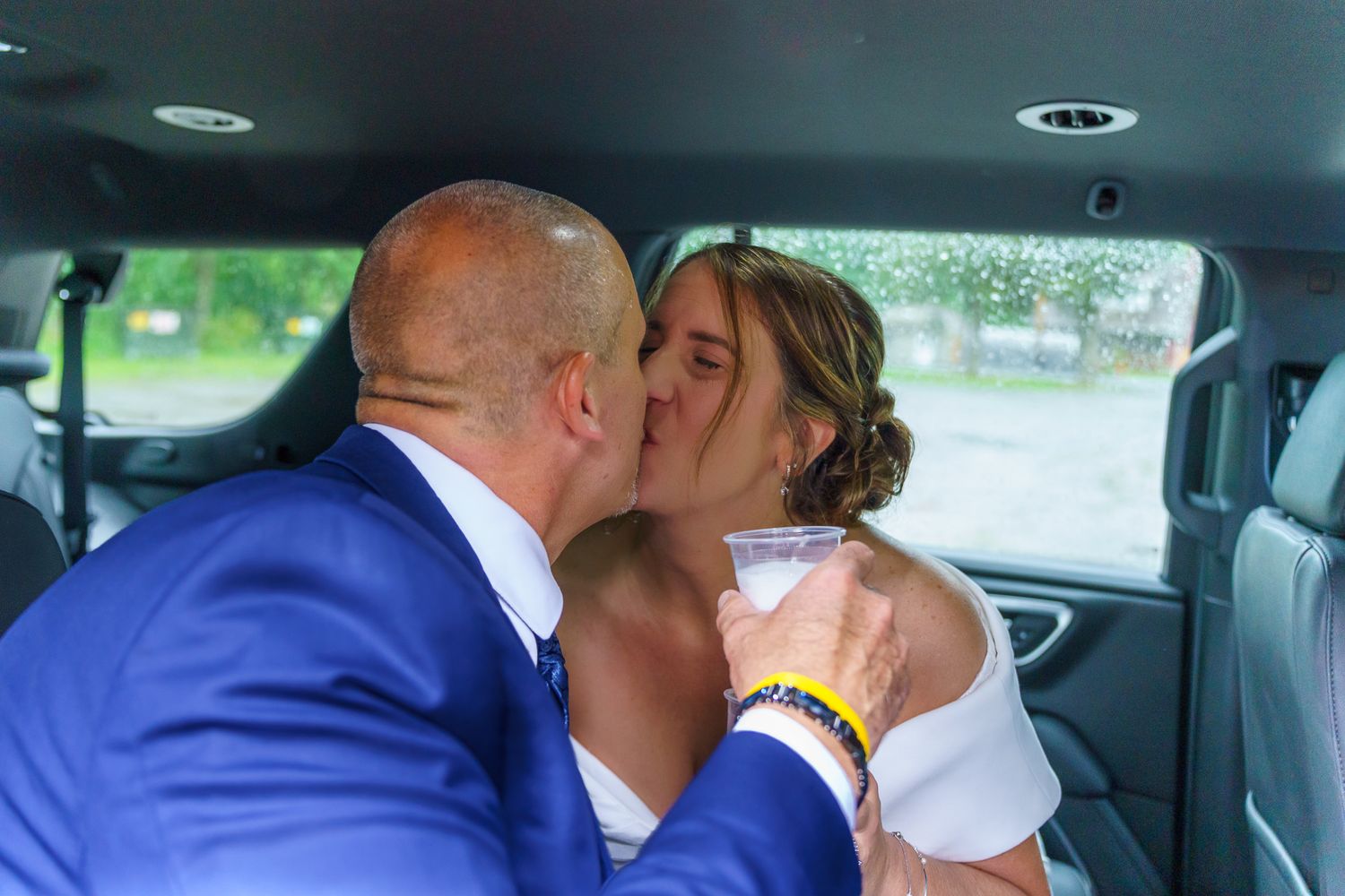Bride and groom sharing a romantic kiss inside a limousine on their wedding day.
