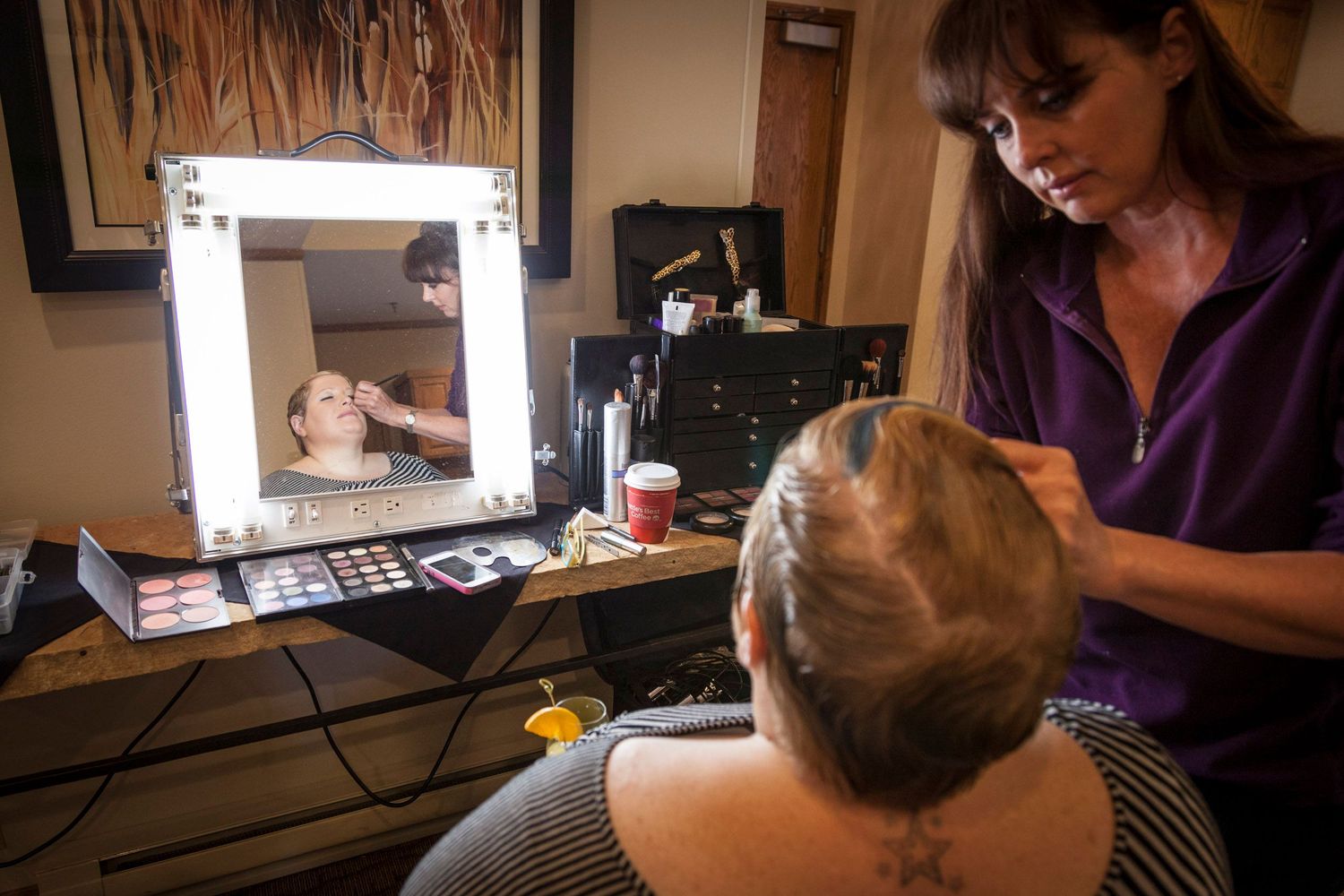 Professional makeup artist applying cosmetics to a client in front of a lighted vanity mirror in a salon.