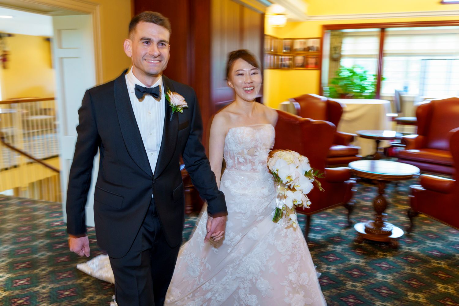 Bride in lace gown and groom in black tuxedo walking together at elegant wedding venue.