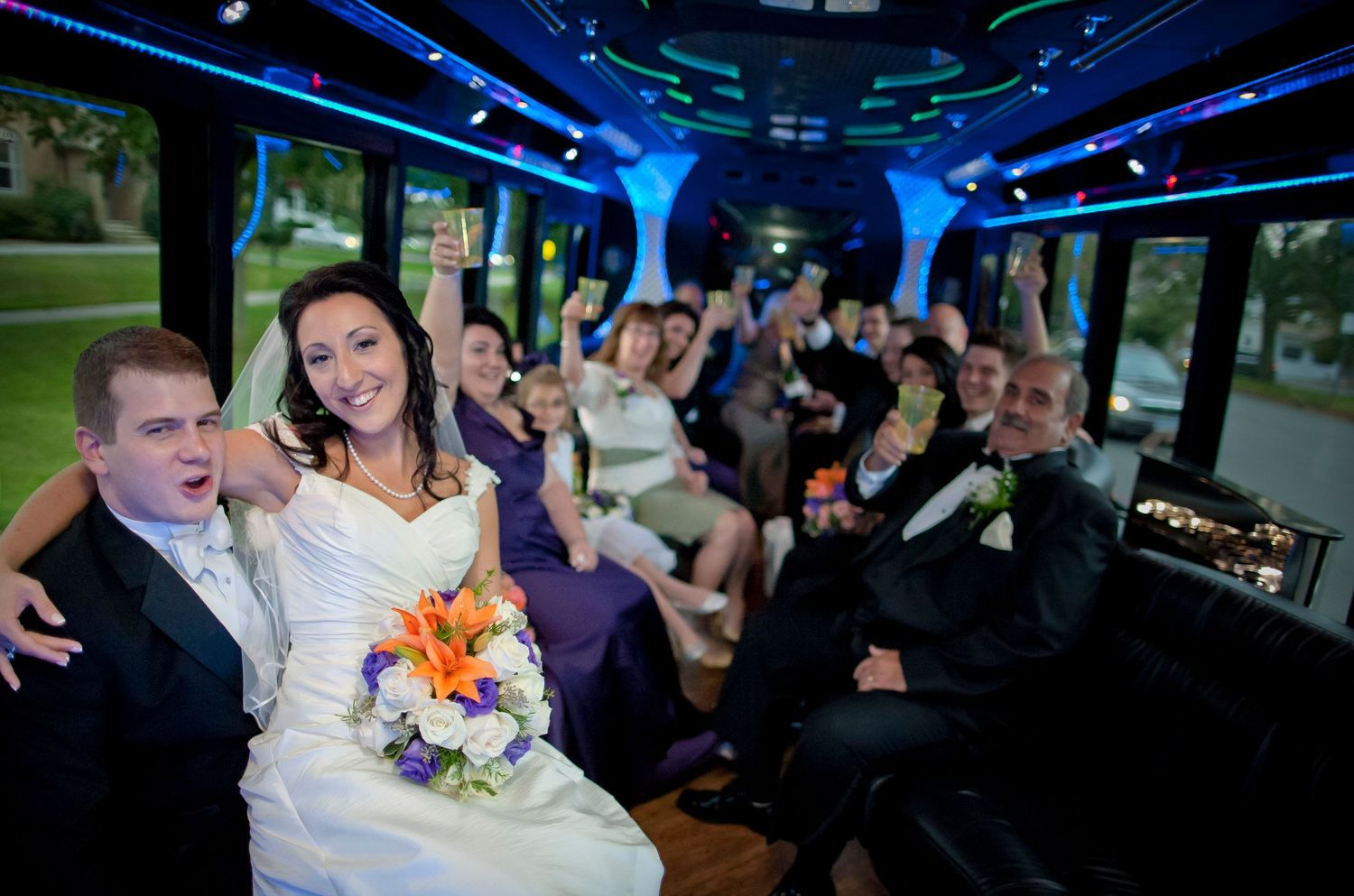 A bride and groom celebrating with their wedding party inside a party bus.