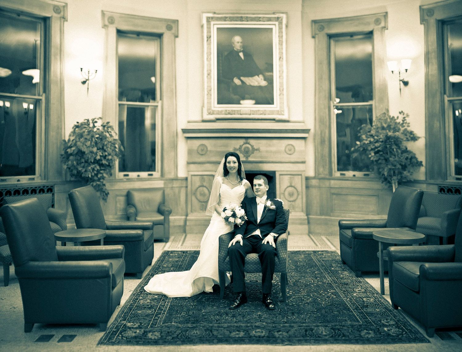 Elegant bride and groom posing in grand formal room beneath classic portrait painting.